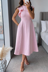 Woman wearing a pink midi dress with cap sleeves and a pleated skirt, posing by a window with a bed in the background.