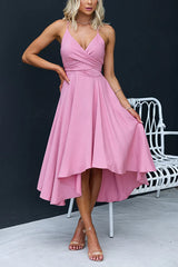Woman wearing a pink high-low midi dress with a cross-over neckline, posing with her hand on her hip.