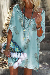 woman wearing a light blue pineapple print kaftan dress with lace trim, layered necklaces, and a colorful tasseled clutch