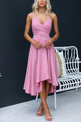 Woman wearing a pink high-low midi dress with a cross-over neckline and tie waist, standing next to a white chair.