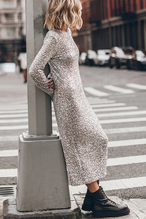 Woman leaning against a pole in a silver sequined midi dress with long bell sleeves and black combat boots.