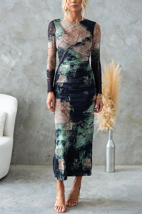 Woman wearing a long-sleeved, abstract print midi dress with ruched detailing, standing in a room with a concrete wall.