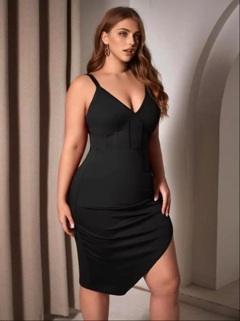 A plus-size woman in a black V-neck, spaghetti strap dress with a corset detail and an asymmetrical hem with a thigh slit, posing with hands on hips.