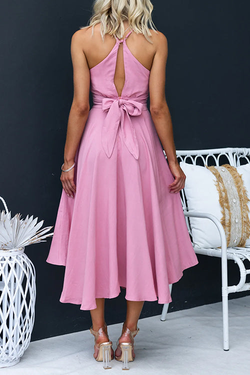 Back view of a woman in a pink high-low midi dress with an open back and tie detail.