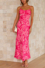 A woman stands facing forward, wearing a long, pink floral print dress with spaghetti straps and a ruched bodice.