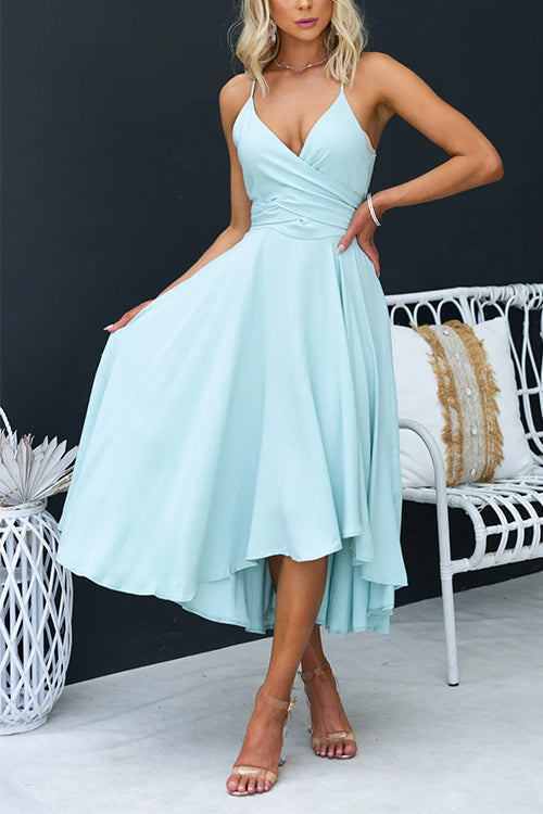 Woman wearing a light blue high-low midi dress with a cross-over neckline, standing next to a white chair.