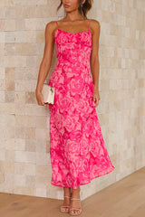 A woman poses with her hand on her hip, wearing a long, pink floral print dress with spaghetti straps and a ruched bodice.
