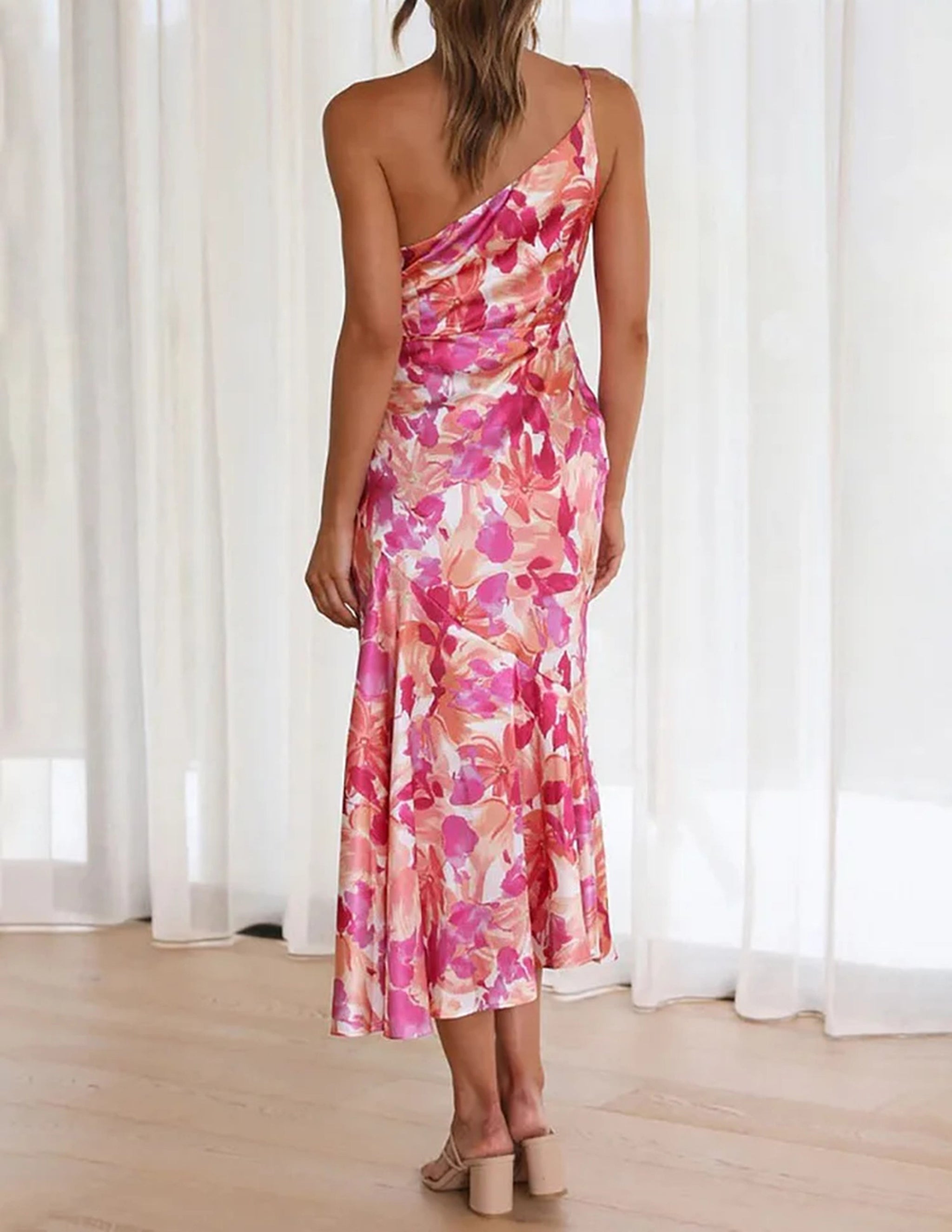 The back of a woman wearing a pink and orange floral print one-shoulder satin dress.