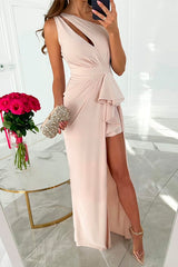 A woman in a light pink one-shoulder maxi dress with a high slit and ruffle detail, holding a sparkling clutch.