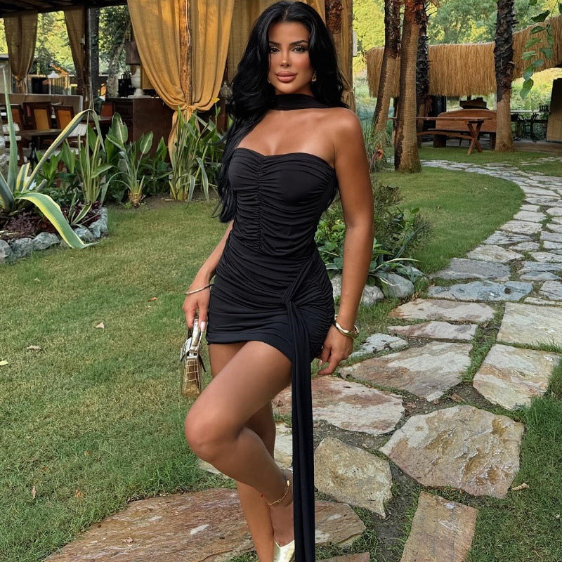 Full body shot of a woman in a black strapless ruched mini dress with a gold clutch and heels, standing in a garden with a stone path.