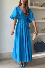 Woman wearing a vibrant blue maxi dress with puff sleeves and a V-neck, holding a gold clutch.