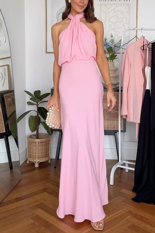 A woman in a pink maxi dress with a halter neckline and a pearl-embellished clutch.