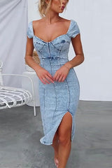 woman wearing a light blue denim sheath dress with a sweetheart neckline, cap sleeves, a high slit, and corset detailing