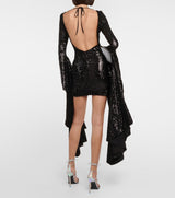 back view of a woman wearing a black sequined mini dress with long bell sleeves and an open back with a tie closure