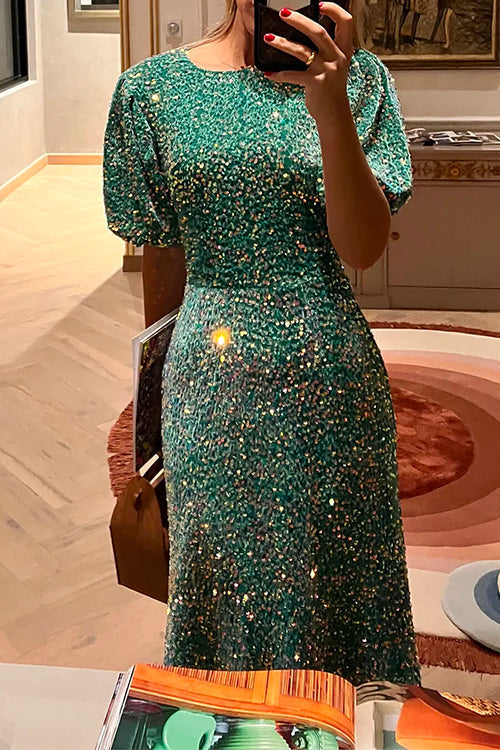 A woman in a sparkling green sequined midi dress with puff sleeves, holding a phone and a brown purse.