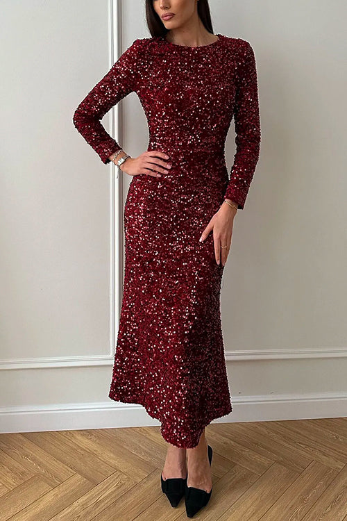 Woman in a long-sleeved, floor-length red sequined dress with a mermaid hem, standing against a white wall.