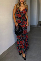 Woman wearing a long, floral print dress with red roses and purple flowers on a black background, holding a black woven handbag.
