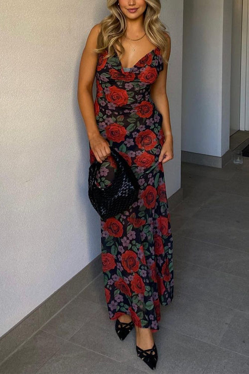 Woman wearing a long, floral print dress with red roses and purple flowers on a black background, holding a black woven handbag.