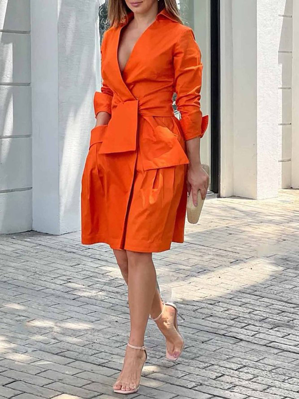 woman wearing an orange wrap dress with a tie waist and pleated skirt and heels