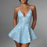 A woman in a light blue floral jacquard mini dress with a plunging V-neckline and spaghetti straps poses against a grey background.