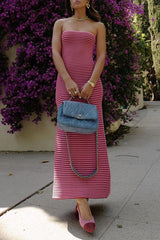 Woman wearing a pink and red striped strapless maxi dress, holding a blue quilted handbag and wearing pink heels