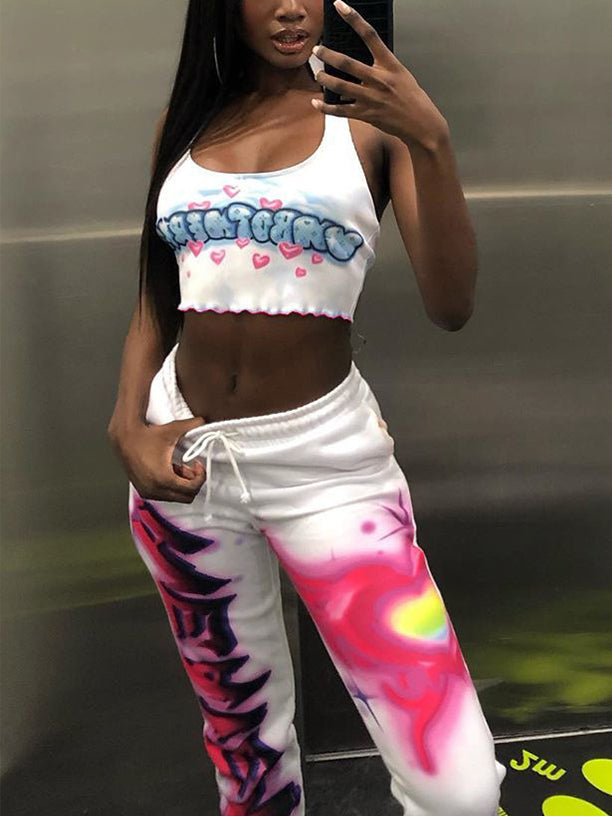 A woman wearing a white halter neck crop top with a blue and pink graphic print and pink hearts, paired with white sweatpants with colorful graphic print.