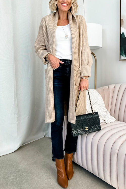 woman wearing a long beige knit cardigan over a white top and dark wash jeans