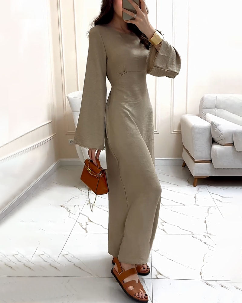 Side profile of a woman wearing a beige dress with bell sleeves and brown sandals, holding a brown handbag.