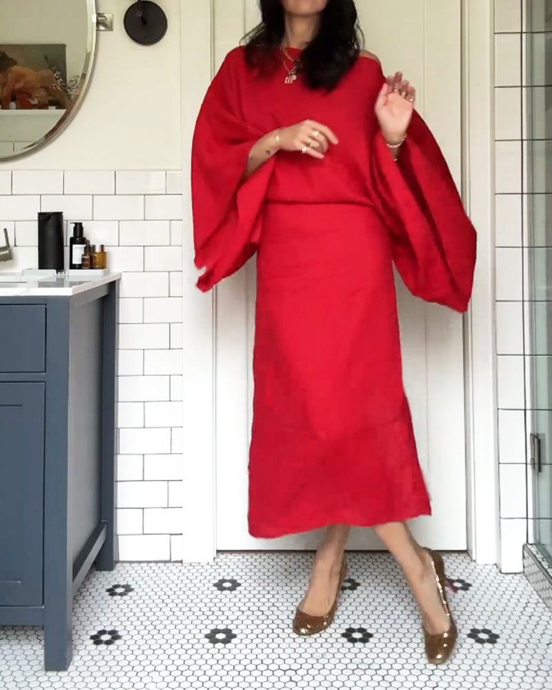 Woman in a red linen dress with kimono sleeves and gold heels, posing in a bathroom.
