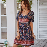 Woman wearing a navy floral print mini dress with puff sleeves and a tie neck
