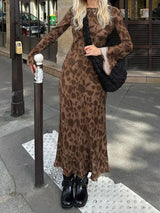 A woman wearing a long-sleeved brown floral print maxi dress and black boots standing on a sidewalk.