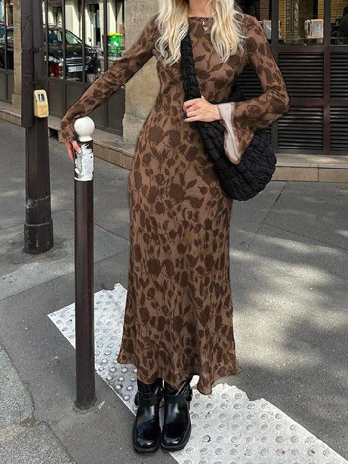 A woman wearing a long-sleeved brown floral print maxi dress and black boots standing on a sidewalk.
