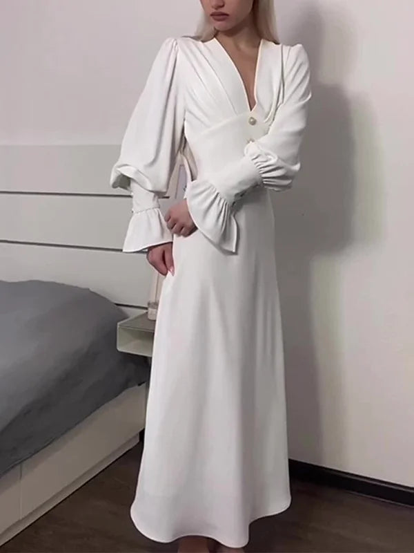 Woman wearing a long-sleeved white dress with puffed sleeves and a V-neckline.