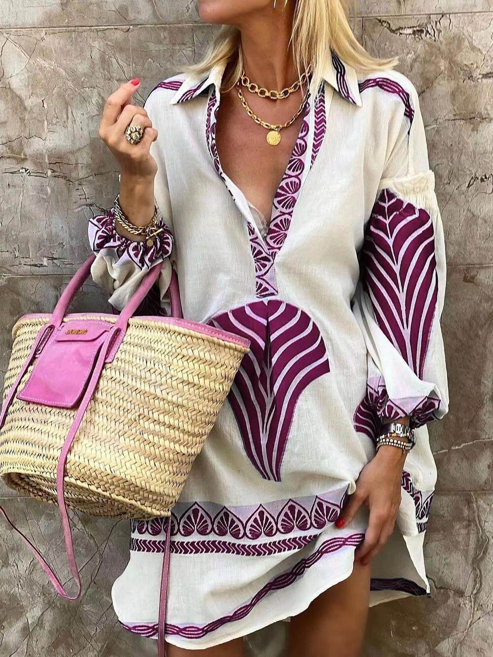 A woman models a white shirt dress with a purple leaf print, a straw bag, and gold jewelry.