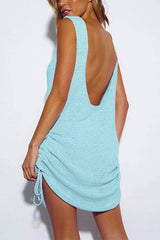 Woman wearing a light blue knit mini dress with drawstring details on the side, showing the back with a low scoop neckline.