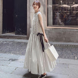 Woman wearing a long white sleeveless dress with black vertical stripes and a black ribbon tie at the waist, holding a white shopping bag and smiling at the camera.