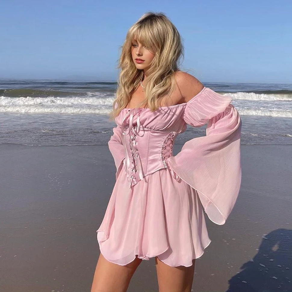 Woman on the beach wearing a pink off-the-shoulder dress with a corset bodice and bell sleeves