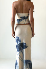 Woman wearing a cream strapless top with a blue floral print and a matching cream maxi skirt with a blue floral print, viewed from the back.