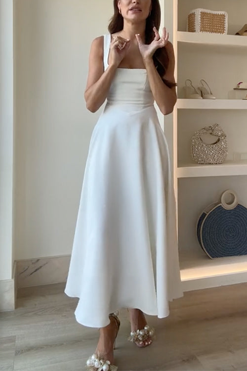 A woman gestures with her hands while wearing a white midi dress.