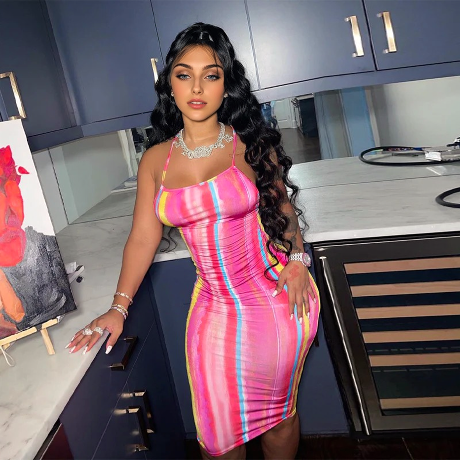 Woman in a pink, yellow, and blue striped bodycon midi dress with spaghetti straps and a cowl neckline, accessorized with jewelry.