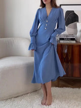 Woman wearing a long-sleeved blue dress with puffed sleeves and a V-neckline, holding the skirt.
