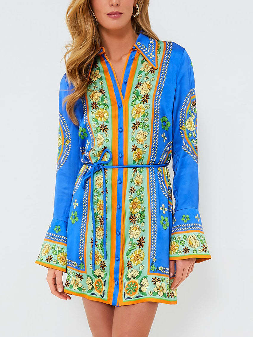 A woman models a blue shirt dress with a vibrant floral print and orange trim.