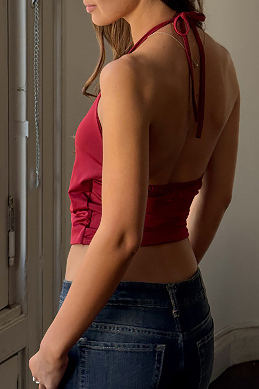 woman wearing a red halter neck wrap top with a silver ring detail and blue denim jeans, back view
