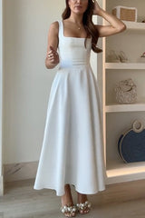 A woman poses in a white square-neck dress and pearl shoes.