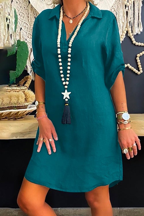 Woman wearing a teal collared V-neck short sleeve A-line dress with a long beaded necklace with a star and tassel pendant.