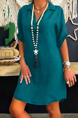 Woman wearing a teal collared V-neck short sleeve A-line dress with a long beaded necklace with a star and tassel pendant.