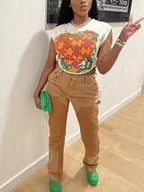 Full body shot of a woman in a white graphic t-shirt and brown distressed pants