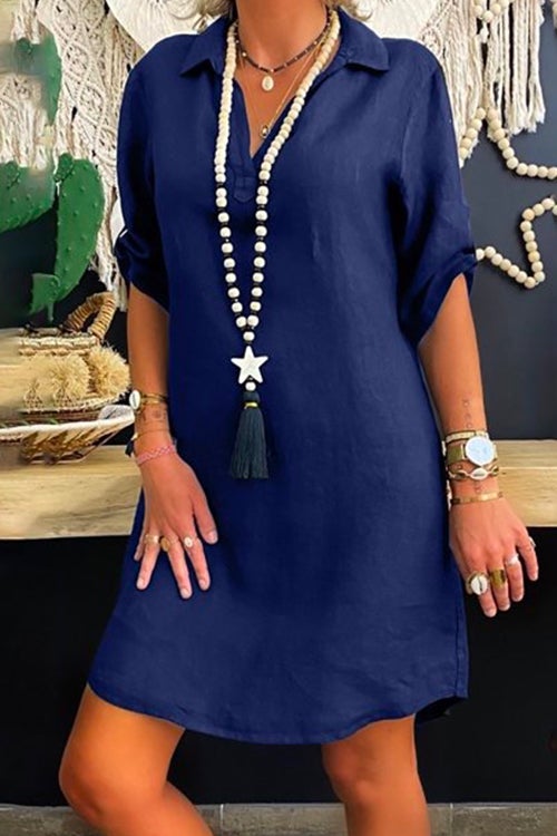 Woman wearing a navy blue collared V-neck short sleeve A-line dress with a long beaded necklace with a star and tassel pendant.