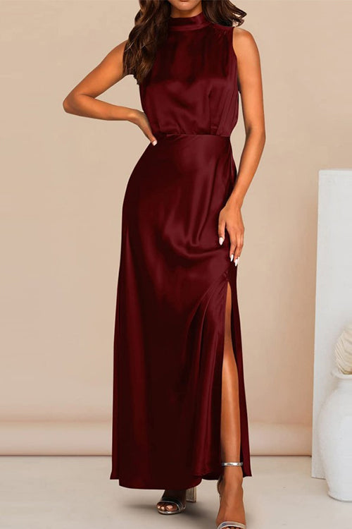 Woman wearing a maroon satin maxi dress with a high neckline, sleeveless design, and a high slit on the leg, standing against a light background.