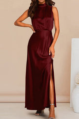 Woman wearing a maroon satin maxi dress with a high neckline, sleeveless design, and a high slit on the leg, standing against a light background.